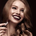 Beautiful blonde in a Hollywood manner with curls, dark lips, lipstick in hand. Beauty face and hair. Royalty Free Stock Photo