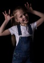 Beautiful blonde little girl on a dark background. She stands in different poses and shows different emotions Royalty Free Stock Photo