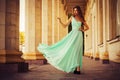 Beautiful blonde with a long curly hair in a long evening dress in static outdoors near retro vintage building in summer sunset