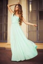 Beautiful blonde with a long curly hair in a long evening dress in static outdoors near retro vintage building in summer sunset Royalty Free Stock Photo