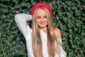 Beautiful blonde with long straight hair in a white sweater and red beret against a wall with ivy leaves. Portrait of a girl Royalty Free Stock Photo