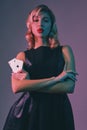Blonde girl in black stylish dress showing two playing cards, posing against colorful background. Gambling entertainment Royalty Free Stock Photo