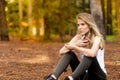 Beautiful blonde model in the middle of pines sitting using cellphone with headset. Listening to music Royalty Free Stock Photo