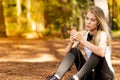 Beautiful blonde model in the middle of pines sitting using cellphone with headset. Listening to music Royalty Free Stock Photo