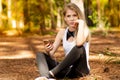 Beautiful blonde model in the middle of pines sitting using cellphone with headset. Listening to music Royalty Free Stock Photo