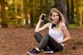 Beautiful blonde model in the middle of pines sitting using cellphone with headset. Listening to music Royalty Free Stock Photo