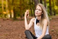 Beautiful blonde model in the middle of pines sitting using cellphone with headset. Listening to music Royalty Free Stock Photo