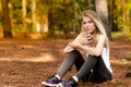 Beautiful blonde model in the middle of pines sitting using cellphone with headset. Listening to music Royalty Free Stock Photo