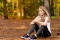 Beautiful blonde model in the middle of pines sitting using cellphone with headset. Listening to music Royalty Free Stock Photo