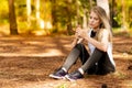 Beautiful blonde model in the middle of pines sitting using cellphone with headset. Listening to music Royalty Free Stock Photo