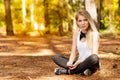 Beautiful blonde model in the middle of pines sitting using cellphone with headset. Listening to music Royalty Free Stock Photo