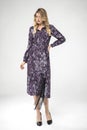 Beautiful blonde model posing in long sleeve, long chic purple dress and black high heels. Royalty Free Stock Photo