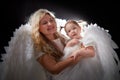 A beautiful blonde mother with curly hair and cute small girl with white wings looking like a nice angels in photo shoot in studio Royalty Free Stock Photo