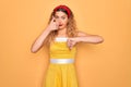 Beautiful blonde pin-up woman with blue eyes wearing diadem standing over yellow background Doing thumbs up and down, disagreement Royalty Free Stock Photo