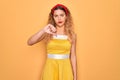 Beautiful blonde pin-up woman with blue eyes wearing diadem standing over yellow background looking unhappy and angry showing Royalty Free Stock Photo