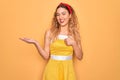 Beautiful blonde pin-up woman with blue eyes wearing diadem standing over yellow background Showing palm hand and doing ok gesture Royalty Free Stock Photo