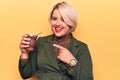 Beautiful blonde plus size woman drinking mate infusion beverage over yellow background smiling happy pointing with hand and