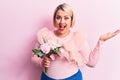 Beautiful blonde plus size woman holding bouquet of pink flowers over isolated background celebrating achievement with happy smile Royalty Free Stock Photo