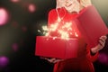 A young blonde in a red dress is tearing off a gift box. From the box there is a bright light and stars.