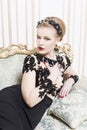 Beautiful blonde royal woman laying on a retro sofa in gorgeous luxury dress. Indoor. Copy Space Royalty Free Stock Photo