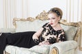 Beautiful blonde royal woman laying on a retro sofa in gorgeous luxury dress. Indoor. Copy Space Royalty Free Stock Photo