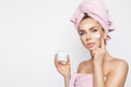 Beautiful blonde woman model holding a cream in her hand and creaming her face with towel on her head Royalty Free Stock Photo