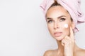 Beautiful blonde woman model holding a cream in her hand and creaming her face with towel on her head Royalty Free Stock Photo