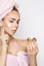 Beautiful blonde woman model holding a cream in her hand and creaming her face with towel on her head Royalty Free Stock Photo