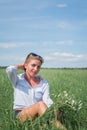 Beautiful blonde short-haired woman in sunglasses sits on a green meadow on a summer day and holds field daisies Royalty Free Stock Photo