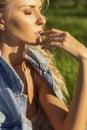 Beautiful blonde slim girl wearing pink lingerie and jeans jacket sits on the grass in the park outdoors. Summer sunny lifestyle Royalty Free Stock Photo