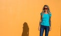 Beautiful blonde in sunglasses look at the camera. Portrait on the background of bright orange wall. Modern hipster girl Royalty Free Stock Photo