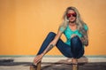 Beautiful blonde in sunglasses posing at the camera. Portrait on the background of bright orange wall. Modern hipster Royalty Free Stock Photo