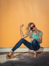 Beautiful blonde in sunglasses posing at the camera. Portrait on the background of bright orange wall. Modern hipster Royalty Free Stock Photo