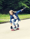 Beautiful blonde teen girl in jeans shirt, on skateboard in park Royalty Free Stock Photo