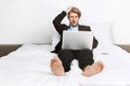 Beautiful blonde unshaved businessman lying in bed, working on laptop computer, holding hand on head with shocked Royalty Free Stock Photo