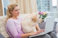 Beautiful blonde using laptop on couch with pet dog Royalty Free Stock Photo