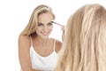 beautiful blonde woman applying mascara in ront of a mirror isolated