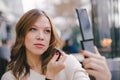 Beautiful blonde woman applying powder on her face for perfect skin using a brush and looking in the mirror Royalty Free Stock Photo