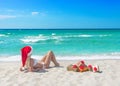 Beautiful blonde woman in bikini, red christmas hat and gift box