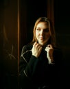 A beautiful blonde woman in a black sweater is sitting on the windowsill near an old window on a dark evening Royalty Free Stock Photo