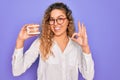 Beautiful blonde woman with blue eyes holding plastic dentrure teeth over purple background doing ok sign with fingers, excellent Royalty Free Stock Photo
