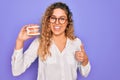 Beautiful blonde woman with blue eyes holding plastic dentrure teeth over purple background happy with big smile doing ok sign, Royalty Free Stock Photo