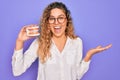 Beautiful blonde woman with blue eyes holding plastic dentrure teeth over purple background very happy and excited, winner Royalty Free Stock Photo