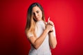 Beautiful blonde woman with blue eyes wearing casual white t-shirt over red background Holding symbolic gun with hand gesture, Royalty Free Stock Photo