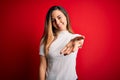 Beautiful blonde woman with blue eyes wearing casual white t-shirt over red background smiling cheerful offering palm hand giving Royalty Free Stock Photo