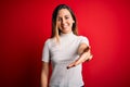 Beautiful blonde woman with blue eyes wearing casual white t-shirt over red background smiling friendly offering handshake as Royalty Free Stock Photo