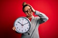 Beautiful blonde woman with blue eyes wearing glasses doing countdown using big clock with happy face smiling doing ok sign with Royalty Free Stock Photo