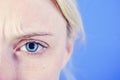 Beautiful blonde woman with clean skin and frekles frown her brows over bright blue background. Thin brows and blue eyes