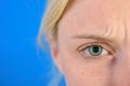 Beautiful blonde woman with clean skin and frekles frown her brows over bright blue background. Thin brows and blue eyes