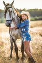 Beautiful blonde woman with curly hair with white hat and horse. Portrait of a girl with denim and her horse. Royalty Free Stock Photo